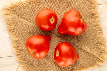 Several red juicy tomatoes with jute napkin on wooden table, macro, top view.