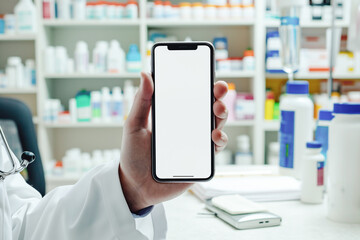 Hand holding smartphone with blank screen in a pharmacy. Blurred shelves of medicine in the background. Concept of healthcare technology and online medical services.