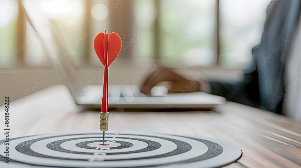 Poster a red dart with a heart-shaped fletching hits the bullseye of a target on a desk in an office settin