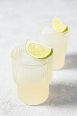 Refreshing lime cocktails on white table. Glass of citrus hard seltzer with ice cube and fresh lime slices. Summer lemonade, mocktail, vitamin water concept. Daiquiri, gimlet, caipirinha