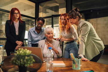 Senior businesswoman with laptop collaborating with interracial team.