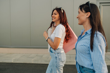 Smiling trendy shopper girls with shopping bags walking on city street