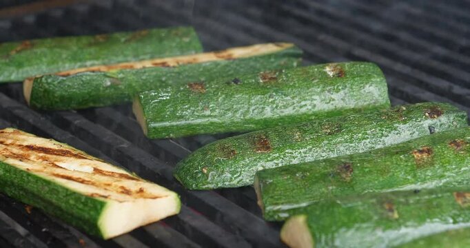 Zucchini or green vegetable marrow are grilled over an open fire. Cook turns the zucchini slices over to ensure even cooking on all sides