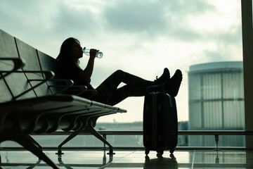Low angle shot of a woman at the airport drinking a bottle of water while waiting for her flight
