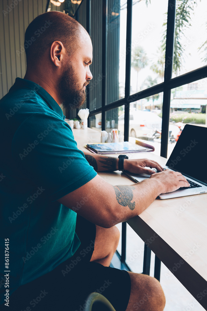 Poster serious male freelancer sitting at table in cafeteria connecting laptop computer to wifi for network