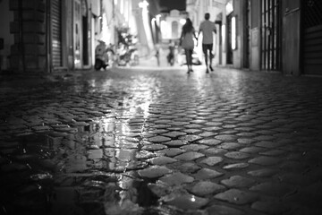 Couple walks away hand in hand aom wet cobbled street in Rome