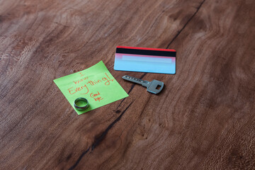 A goodbye note on a wooden table next to a credit card, a key and a ring implying a tragic breakup 