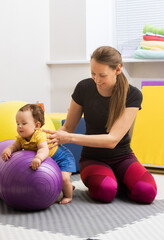 Rehab specialist sitting on purple exercise ball while holding baby patient during motor skills...