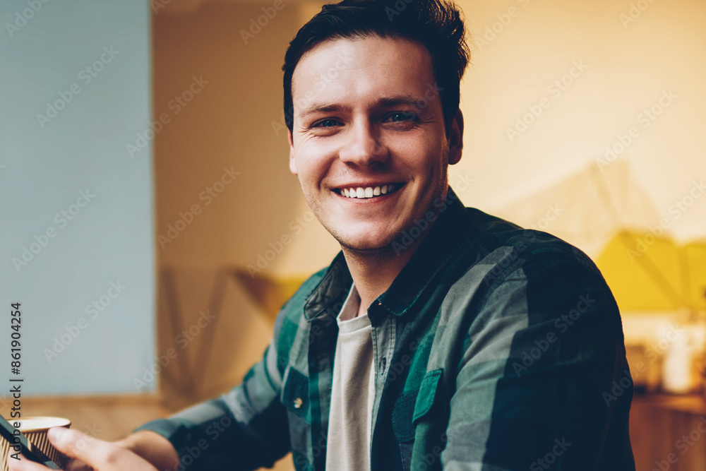 Poster portrait of cheerful hipster guy in casual wear enjoying coffee break chatting via telephone, happy 