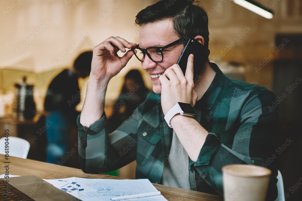 Poster happy young man in eyewear watching webinar on laptop computer making telephone call, cheerful hipst