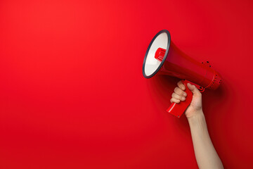 Confident woman holding red megaphone against bold background, symbolizing communication and speaking out with copy space. Amplifying voice for attention-grabbing campaigns