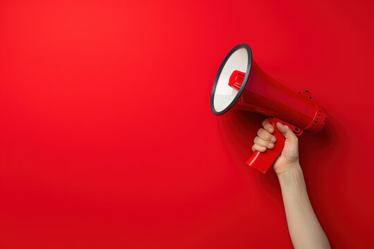 Confident woman holding red megaphone against bold background, symbolizing communication and speaking out with copy space. Amplifying voice for attention-grabbing campaigns
