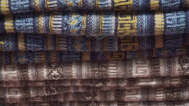 A pile of colorful blankets and scarves are displayed on a table. The colors are bright and cheerful, creating a warm and inviting atmosphere