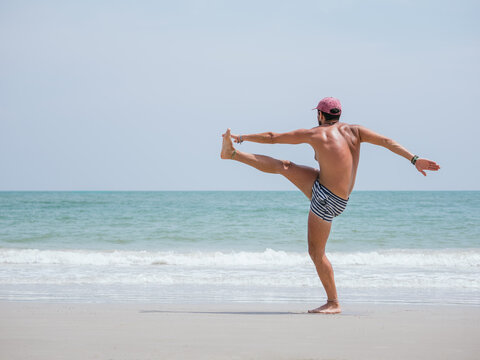 Young Man Balancing on One Leg During Stretching Exercise on Beachfront Getting Ready to Sport. Beach fitness exercise concept - Powered by Adobe