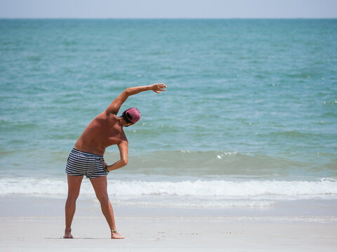 Young Man Performing Stretching Exercises on a Sunny Beachfront - Powered by Adobe