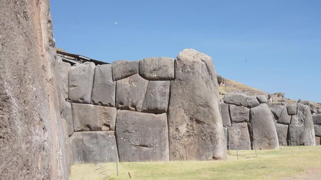 A large rock wall with a blue sky in the background. The wall is made of stone and has a rough texture