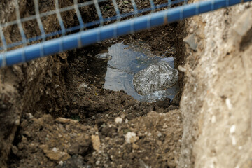 A blue wire fence is above a muddy hole