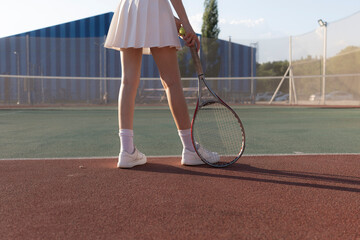 womans legs holding a tennis racket on a clay tennis court, with a tennis ball and the net in the...