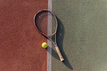 A tennis racquet and ball lie on a clay tennis court, ready for a game