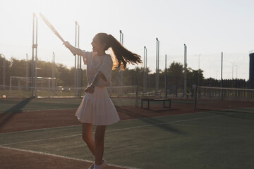 woman in a white tennis outfit celebrates a win with her racket raised high on a green tennis court