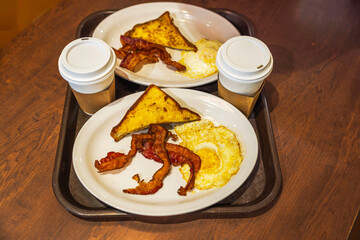 Close-up of a breakfast tray at Miami Airport featuring baked bacon, eggs, and coffee in a disposable cup. 