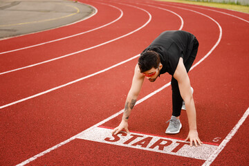 Sporty young man in sunglasses getting ready to run at stadium