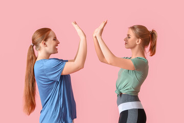Portrait of sporty young women giving each other high-five on pink background