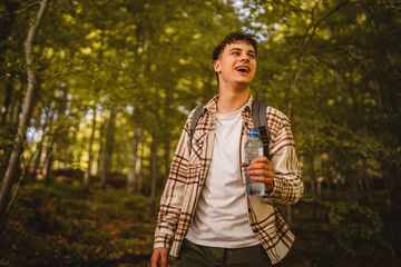 Adult young man walk around forest with backpack hold bottle of water