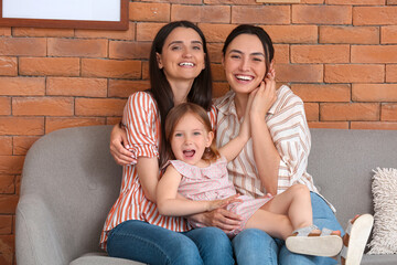 Young lesbian couple with adopted little girl sitting on sofa at home