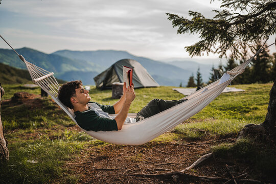 Young boy lying down in a hammock on the mountain and read a book