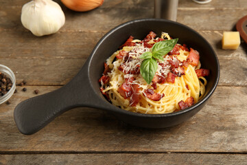 Frying pan with tasty pasta carbonara on wooden background