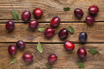Fresh ripe plums and leaves on wooden background