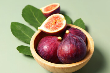 Bowl of ripe fresh figs with plant leaf on green background