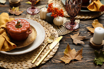Autumn table serving with pot in shape of pumpkin, golden cutlery and dry leaves on wooden table, closeup