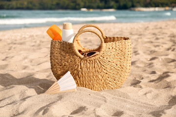 Straw bag with bottles of sunscreen cream and sunglasses on sand