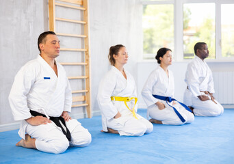 Cosmopolite sportsmen of school oriental martial arts sitting on floor, meditating, mentally...