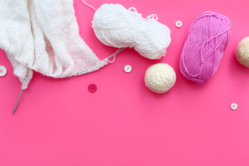Knitting needles, yarn balls and buttons on pink background