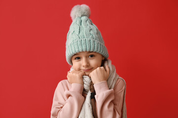 Cute little girl wearing warm hat and scarf on red background