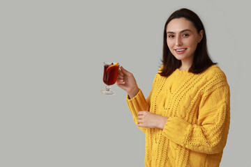 Beautiful young woman with glass cup of hot mulled wine on grey background