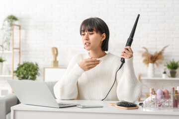 Young female blogger with laptop and curling iron recording video at home