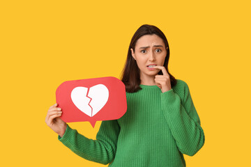 Beautiful young displeased woman with heart dislike icon on yellow background