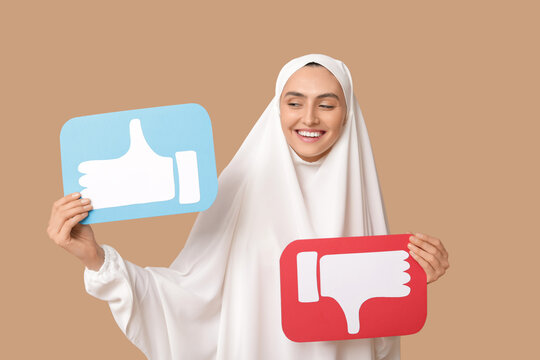 Beautiful young happy Muslim woman with like and dislike icons on beige background