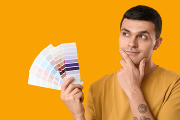 Young man with paint palettes on yellow background