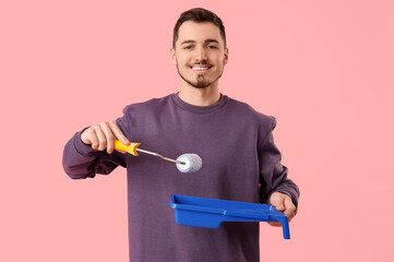 Young man with paint roller and tray on pink background