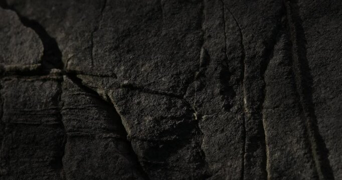 Dolly shot of Dark Rock Surface with Linear Cracks and Textures. 