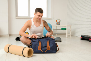 Young man with sports bag and yoga mat in gym