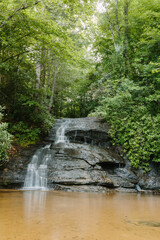 Naklejka premium Beautiful large waterfall between green trees in the mountains. Mountain landscape with a waterfall on a summer day. Wildcat Waterfall, Great Smokey Mountains, South Carolina, USA. 