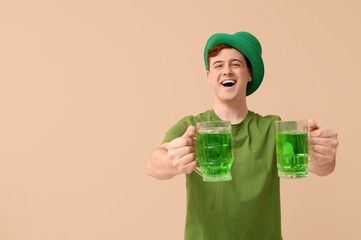 Happy young man in leprechaun's hat with mugs of beer on beige background. St. Patrick's Day...