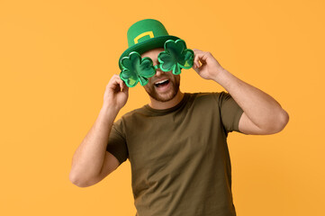 Happy young man in leprechaun's hat with party glasses on yellow background. St. Patrick's Day...
