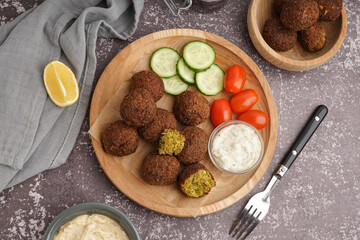 Wooden plate with delicious falafel balls, vegetables and lemon on grunge background